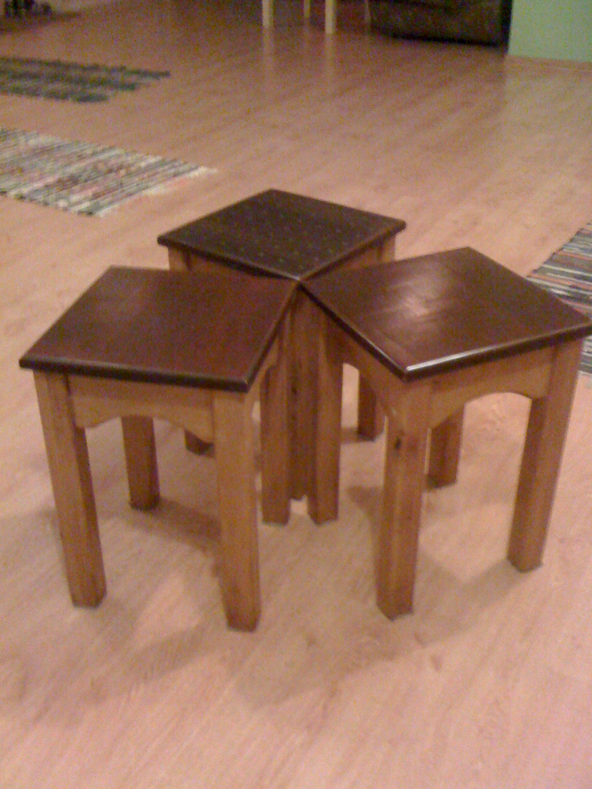 Trzy drewniane stoliki kawowe z ciemnymi blatami, ustawione obok siebie na podłodze w pomieszczeniu.